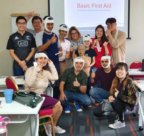 First aid class participants practising bandaging and posing with a CPR manikin