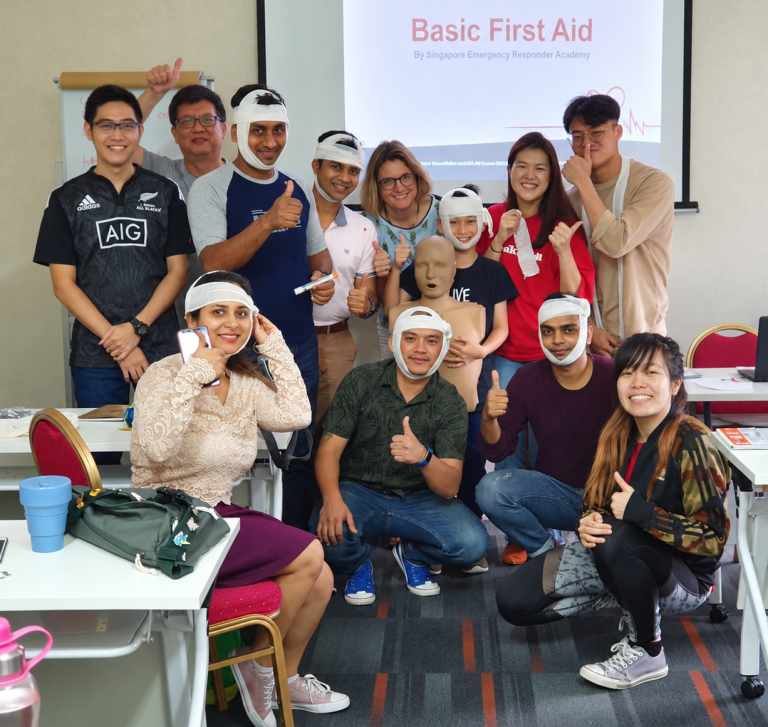 First aid class participants practising bandaging and posing with a CPR manikin